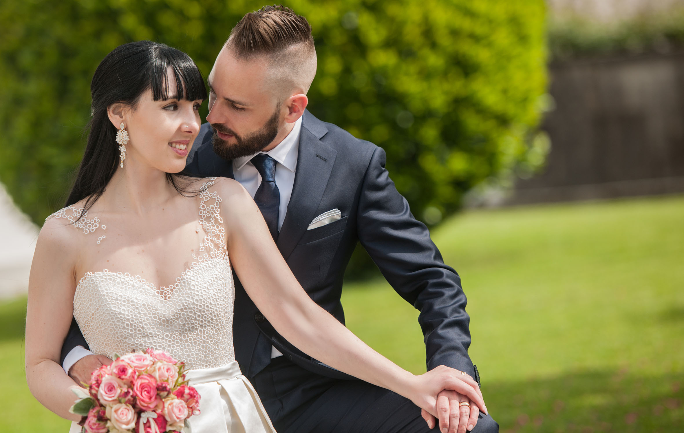 Ramona und Chris Bonbizin in eleganter Gartenkulisse. Chris trägt einen massgeschneiderten Anzug von Scabal, Ramona ein massgefertigtes Kleid aus St.Galler Stickerei, hergestellt im Couture-Atelier der Manufaktur in St.Gallen.