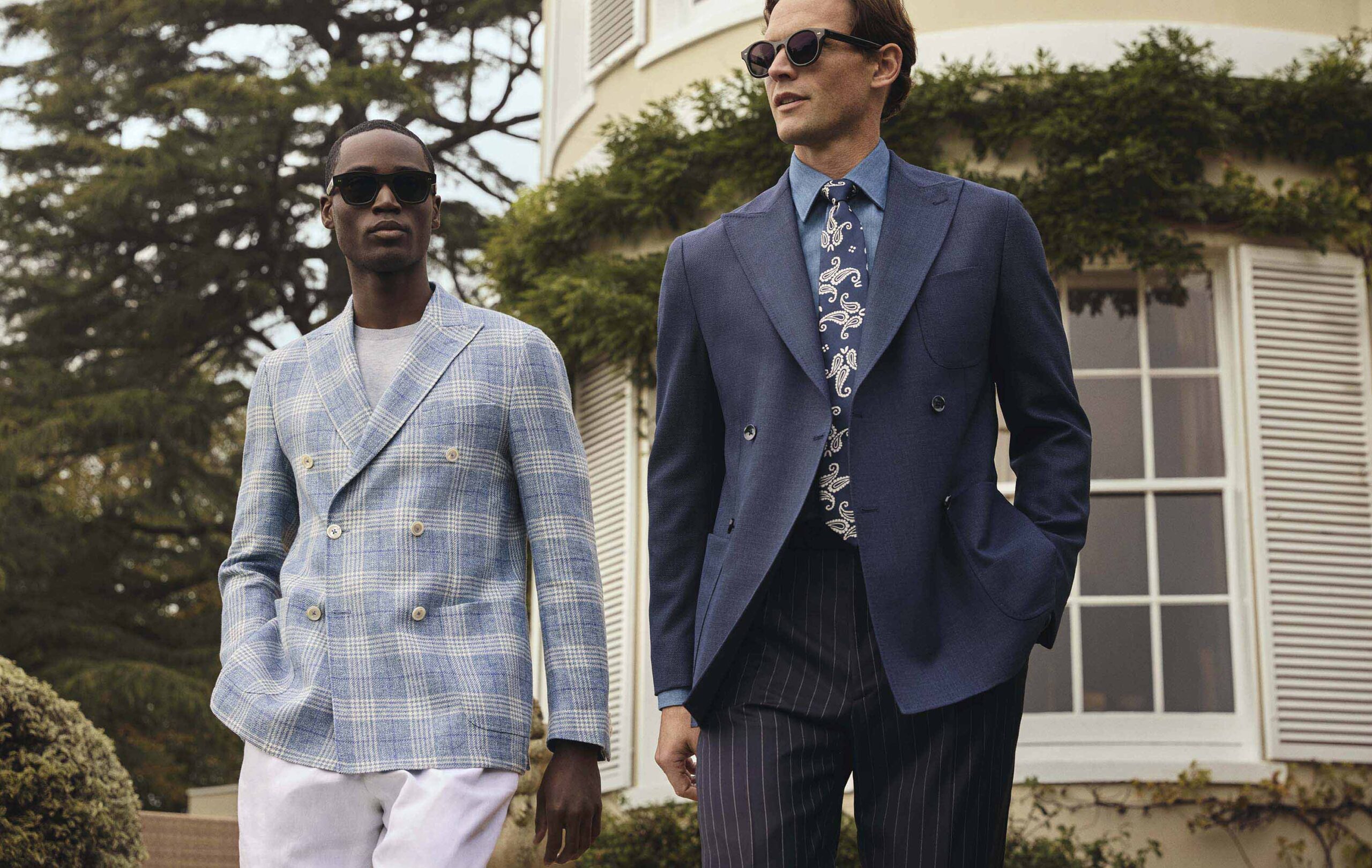 Sakko in Sommerqualitäten aus Seide, Leinen und Wolle von Scabal Zwei stilvolle Männer tragen elegante Sakkos aus Sommerqualitäten mit Materialmix aus Seide, Leinen und Wolle von Scabal, während sie vor einer luxuriösen Villa spazieren.