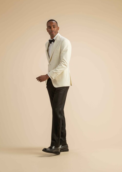 Klassischer Herren-Smoking mit cremeweißem Jackett, schwarzer Fliege und dunkler Hose, getragen von einem Model vor beigem Hintergrund.