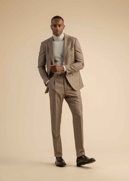 Herrenanzug aus braunem Glencheck-Stoff mit feinem Muster, kombiniert mit einem weissen Rollkragenpullover, getragen von einem Model vor beigem Hintergrund.