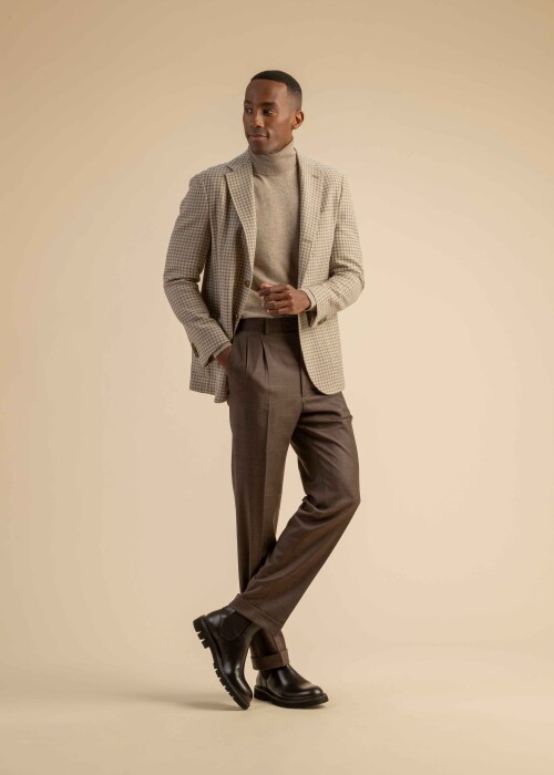 Hahnentritt-Sakko mit Rollkragenpullover aus der Scabal Herbstkollektion Herrenoutfit mit beigefarbenem Hahnentritt-Sakko, hellbraunem Rollkragenpullover und brauner Bundfaltenhose, getragen von einem Model vor beigem Hintergrund.