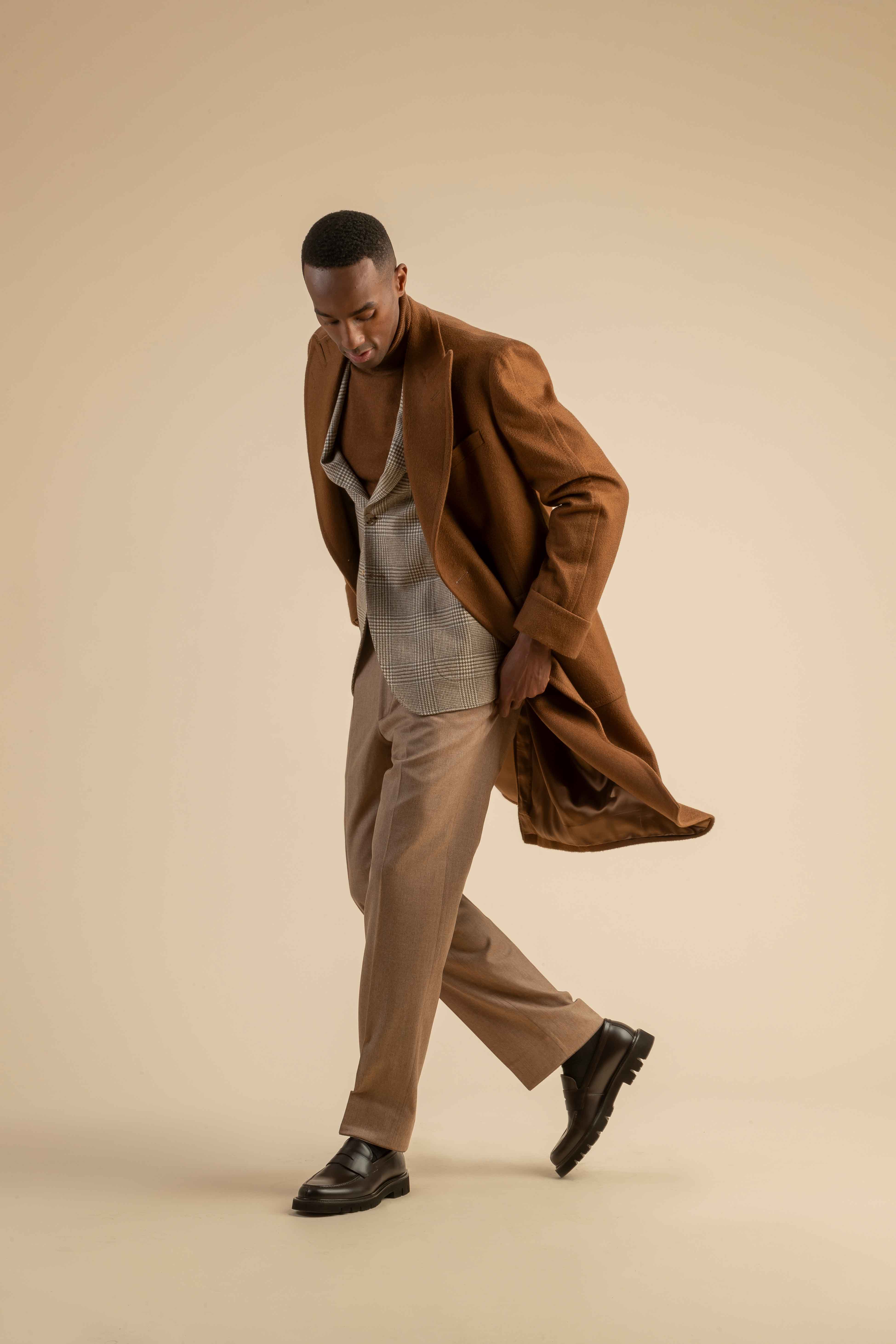 Elegantes Herrenoutfit mit braunem Mantel und Karosakko – herbstlicher Layering-Look Herrenoutfit mit karamellbraunem Mantel über kariertem Sakko, kombiniert mit braunem Rollkragenpullover und beiger Hose.