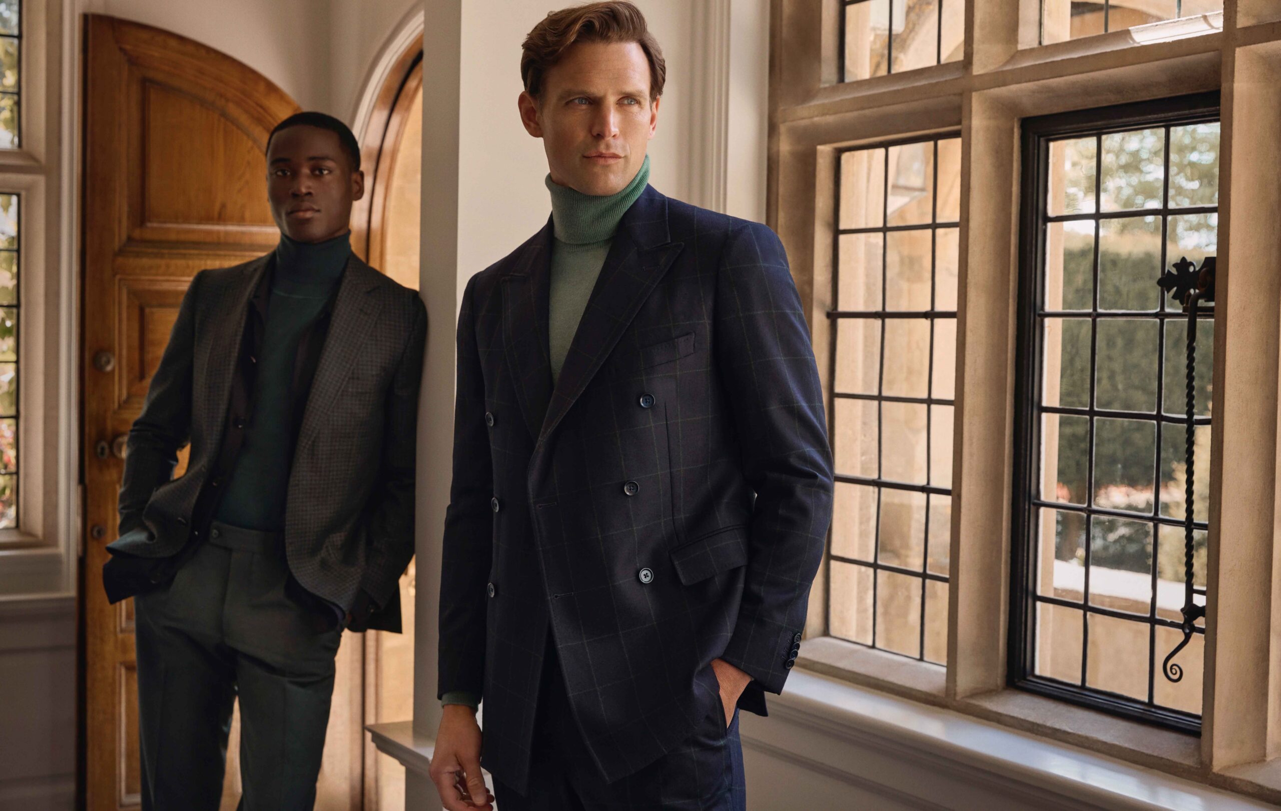 Elegante Herrenanzüge mit Rollkragenpullover für Herbst/Winter – stilvolle Businessmode Zwei Männer in eleganten Herbstanzügen mit Rollkragenpullovern, stehend in klassischem Interieur mit Holz und Sprossenfenstern.