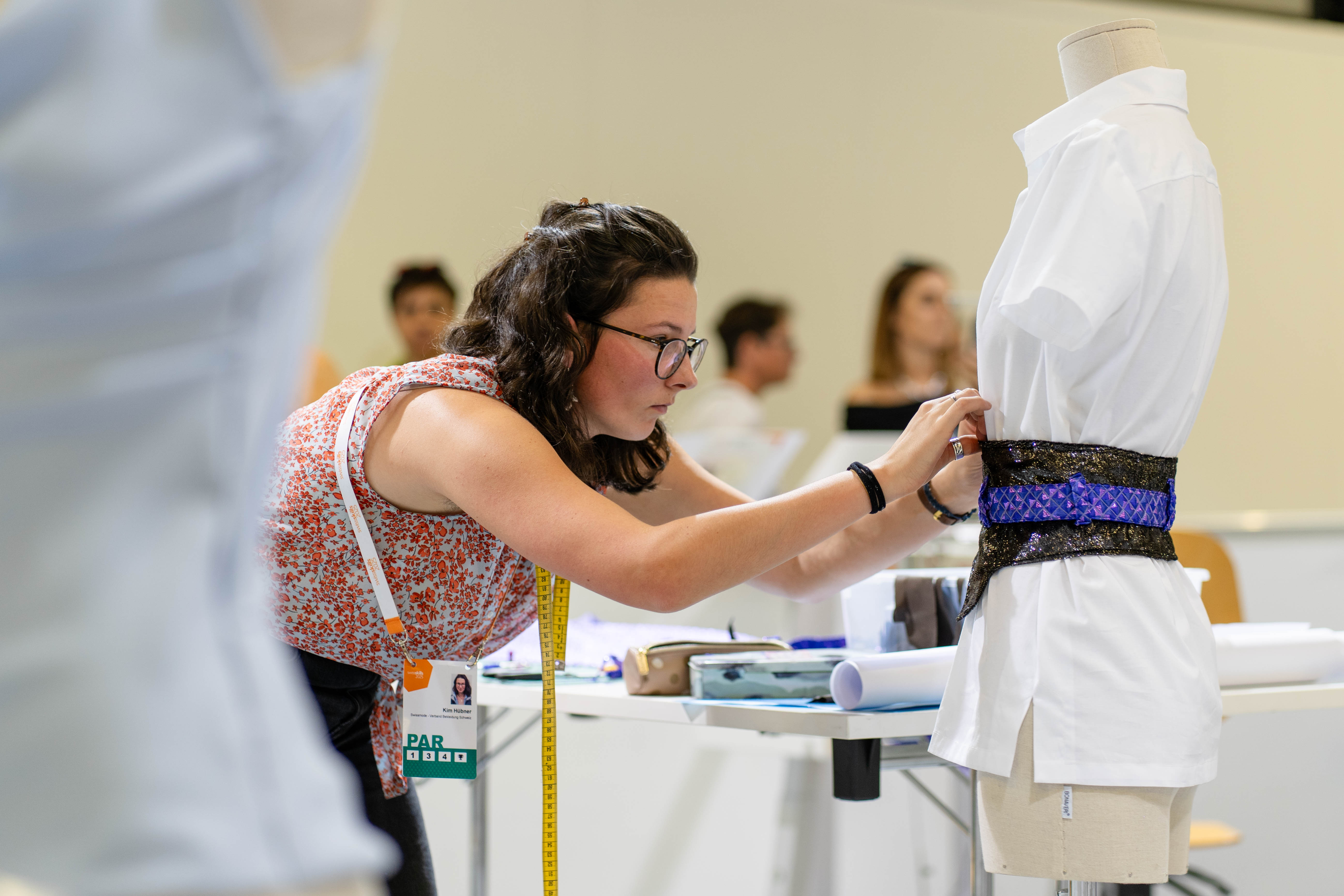 Lernende Bekleidungsgestalterin näht ein Accessoire aus schwarzem und violettem Stoff bei den SwissSkills 2025 in Bern.