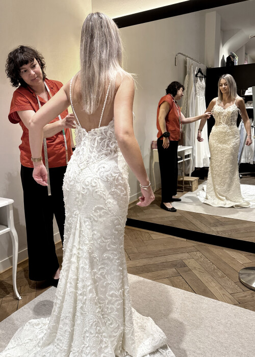 Brautkleid Anprobe in der Manufaktur mit Schneiderin beim Abstecken eines bestickten Meerjungfrau Brautkleides