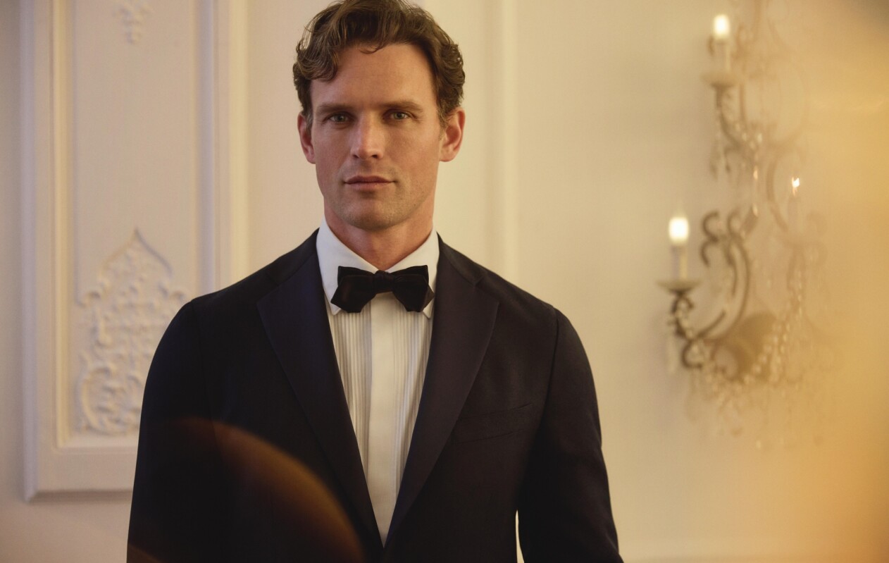 Dieser Hochzeitslook aus der Scabal Jazz Kollektion verbindet sommerliche Leichtigkeit mit festlichem Stil. Das pinke Sakko mit feiner Textur, kombiniert mit einer tief bordeauxfarbenen Hose, schafft einen mutigen und dennoch raffinierten Auftritt – ideal für besondere Anlässe.