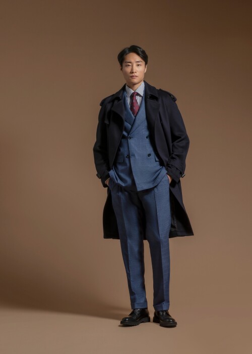 Blauer massgeschneiderter Dreiteiler mit Krawatte und dunkelblauem Trenchcoat aus der Scabal Herbst-Winter Kollektion 2027, erhältlich bei Die Manufaktur – deine Schneiderei in St. Gallen.
